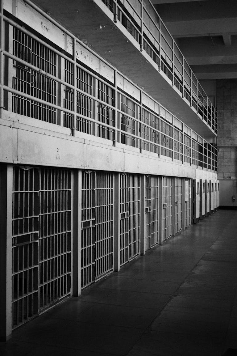 Monochrome image of an empty prison row with steel bars and walkways.